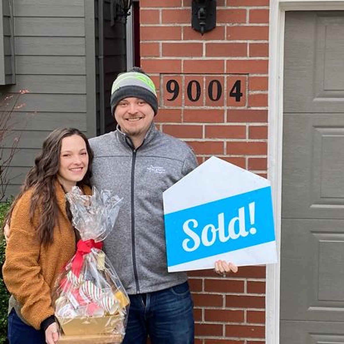 A couple celebrating with a Sold sign outside their new Portland home.