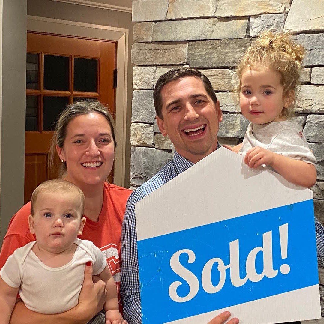 A young family celebrating with a Sold sign on closing day.